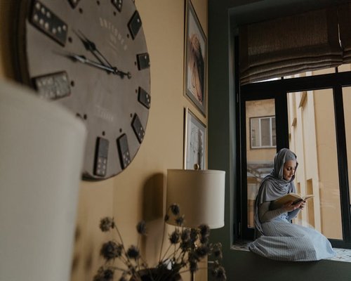 A woman reading a book comfortably while sitting near a large window with soft daylight